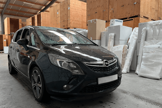 Auto in voertuigopslag binnen een beveiligde opslagruimte met houten opslagboxen en verpakte goederen.