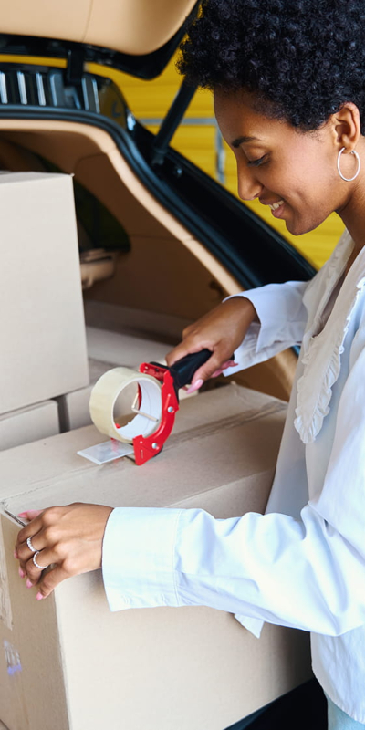 Vrouw pakt verhuisdozen in bij de open kofferbak van een auto in